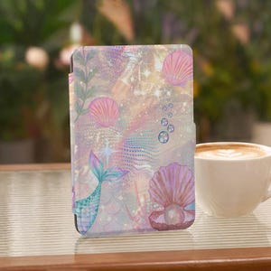 Puede incluir: Una funda rectangular para lector electrónico con un tema submarino en tonos pastel, que muestra una cola de sirena, conchas rosas, una perla dentro de una concha abierta y burbujas. El diseño incluye destellos estelares y escamas.