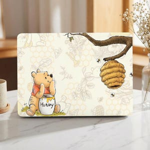 May include: A rectangular laptop skin featuring Winnie the Pooh with a honey pot labelled "Hunny". The background is cream-coloured with a honeycomb pattern, bees, and a beehive hanging from a tree branch. The design is a cartoon illustration.