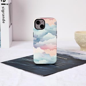 Peut inclure: Une coque de smartphone avec un motif aquarelle d'un ciel pastel avec des nuages roses, bleus et blancs. La coque a une finition brillante et un module caméra noir.