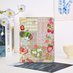 Pode incluir: Uma capa de tablet colorida com um design de patchwork com morangos, borboletas e outras ilustrações caprichosas. A capa tem uma variedade de cores e padrões pastel, incluindo xadrez vichy e estampas florais. O tema geral é fofo e divertido.