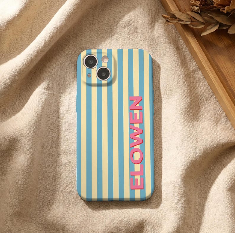 Puede incluir: Funda de tel&eacute;fono con un patr&oacute;n de rayas verticales en azul claro y amarillo. La palabra "FLOWEN" est&aacute; impresa verticalmente en rosa. La funda tiene un recorte para la c&aacute;mara en la parte superior.