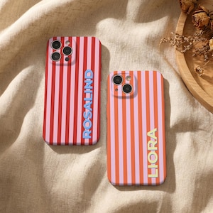 Puede incluir: Dos fundas de tel&eacute;fono con rayas verticales. Una funda es roja y rosa con el nombre "ROSALIND" en azul. La otra funda es naranja y rosa con el nombre "LIORA" en amarillo. Ambas fundas tienen un recorte para la c&aacute;mara.