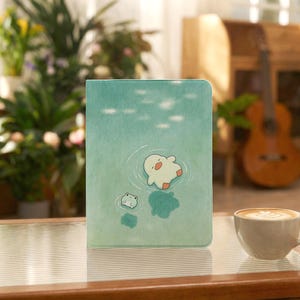 Könnte beinhalten: Eine rechteckige Tablethülle mit hellgrünem Aquarellhintergrund, auf der eine weiße Ente und ein kleiner grüner Frosch im Wasser schwimmen. Das Design zeigt Wellen um die Figuren und sanfte weiße Lichtreflexe auf der Wasseroberfläche.