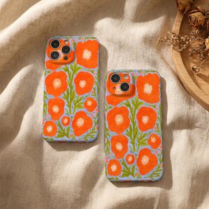Puede incluir: Dos fundas para tel&eacute;fono con un vibrante estampado floral de amapolas de color naranja brillante y tallos verdes sobre un fondo azul b&iacute;garo claro. Las fundas tienen aberturas para las lentes de la c&aacute;mara y un acabado mate suave.