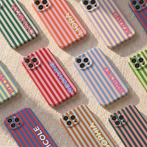 Può includere: Una collezione di custodie per telefoni colorate con motivi a righe verticali. Ogni custodia presenta un nome diverso in un colore coordinato. Le custodie sono in vari colori, tra cui rosso, blu, verde, arancione e viola.