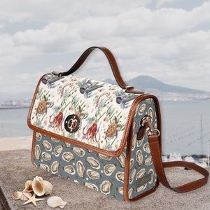 May include: A brown leather handbag with a white and blue patterned design featuring sea life, including sea turtles, an octopus, and seashells. The bag has a top handle and a long adjustable shoulder strap.