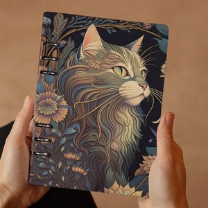 Può includere: Un taccuino con motivi neri e dorati con un'illustrazione dettagliata del viso di un gatto. Il gatto ha gli occhi verdi e un naso bianco.
