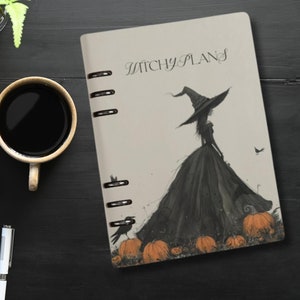 May include: A beige planner with a black and white illustration of a witch with a black dress and a pointed hat. The text "Witchy Plans" is printed on the cover. The background features pumpkins and a crow.