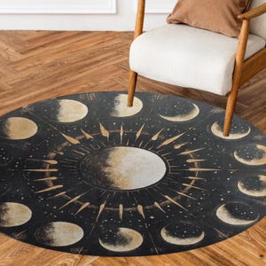 Pode incluir: Um tapete redondo preto e dourado com um design de sol e lua. O sol está no centro do tapete e é cercado por um anel de luas em diferentes fases.