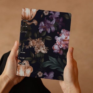 Könnte beinhalten: Ein schwarzer Ordner mit floralem Muster und silbernen Ringen. Der Ordner hat einen dunklen Hintergrund mit rosa, lila und cremefarbenen Blumen.