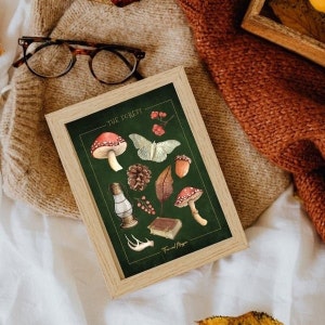 May include: A framed print with a green background featuring illustrations of forest elements, including mushrooms, a moth, a pine cone, a leaf, berries, a lantern, a book, and antlers. The text "THE FOREST" and "Fae and Magic" are printed on the print.