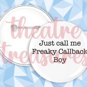 May include: Two white round badges. One has a pin back and the other has the text "Just call me Freaky Callback Boy" in black font. The background is a light blue and white geometric pattern.