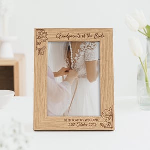 May include: A light oak picture frame with the inscription "Grandparents of the Bride" and floral designs. The frame contains a wedding photo. The date of the wedding is also engraved on the frame.