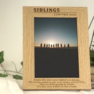 May include: A wooden picture frame with a silhouette photo of people standing on a beach at sunset. The frame has an engraved inscription that reads "Siblings ['sib.lings] noun. People who share your memories & dreams. The closest people to you; truly unique relationships. They are loved greatly by Jordan. See also: Gina & Rebecca, best friends."