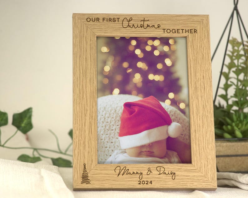 Pu&ograve; includere: Una cornice per foto in legno con un'iscrizione personalizzata che recita "Il nostro primo Natale insieme" e "Mamma & Daisy 2024". La cornice presenta una foto di un bambino che indossa un cappello rosso di Babbo Natale.