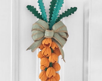 May include: A handmade crochet carrot-shaped door hanger. The carrot features orange tulip-shaped flowers, green stems, and a decorative bow with a gingham pattern. The door hanger is designed to be hung on a door.