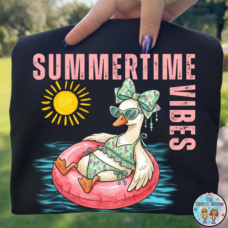 Puede incluir: Camiseta negra con la frase "SUMMERTIME VIBES" en rosa. Un dibujo de un ganso con gafas de sol y bikini flota en un flotador rosa. Tambi&eacute;n hay un sol amarillo.