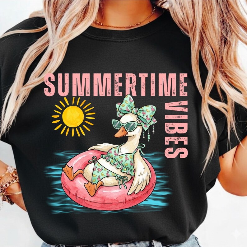Puede incluir: Camiseta negra con un dise&ntilde;o de un ganso con gafas de sol, un lazo y un traje de ba&ntilde;o, flotando en un flotador rosa. Las palabras "SUMMERTIME VIBES" y un sol amarillo tambi&eacute;n est&aacute;n presentes.