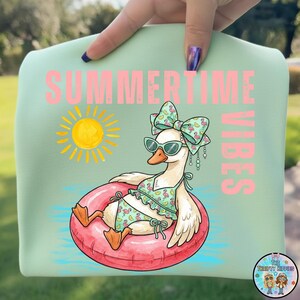 Puede incluir: Camiseta verde claro con un dibujo de un ganso de dibujos animados con gafas de sol y un traje de ba&ntilde;o, flotando en una boya rosa. La camiseta tiene las palabras "SUMMERTIME VIBES" en rosa y un sol amarillo.