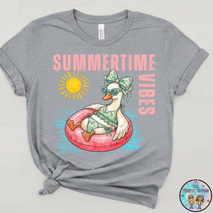 Puede incluir: Camiseta gris con un gr&aacute;fico de un ganso con gafas de sol y un traje de ba&ntilde;o, flotando en una boya rosa. Las palabras "SUMMERTIME VIBES" est&aacute;n impresas encima del ganso y el sol.