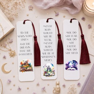 May include: Three rectangular white bookmarks with dark red tassels. Each features black printed text and a colourful watercolour illustration at the bottom. The text reads: To the stars who listen, Never again would she be weak, and You do not fear.
