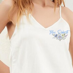 May include: White tank top with a blue floral design and the text "Mrs. Roberts" on the front.