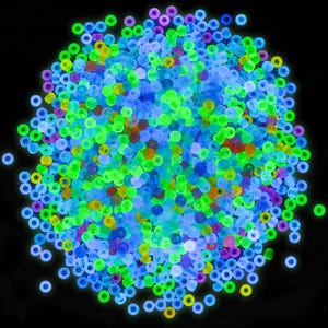May include: A large collection of small, round, translucent beads in vibrant neon colors including lime green, bright blue, purple, and yellow. These tiny circular beads are scattered in a dense, circular cluster against a solid black background.