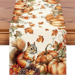 May include: A rectangular table runner featuring a printed pattern of orange pumpkins, brown pinecones, and scattered autumn leaves in shades of yellow, orange, and brown. A squirrel with a bushy tail is positioned among the pumpkins.