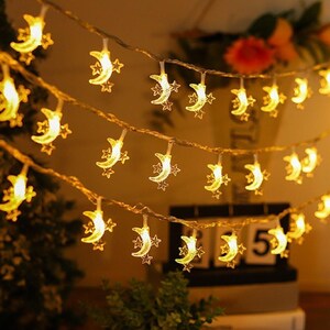 May include: A string of LED fairy lights featuring translucent crescent moon and star shapes. The lights emit a warm yellow glow and are arranged in multiple horizontal strands, creating a decorative illumination effect with clear plastic wiring.