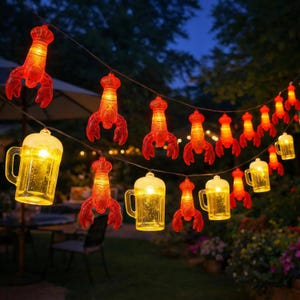 May include: A string of decorative LED lights featuring alternating translucent orange lobster-shaped covers and clear yellow beer mug-shaped covers. Each light fixture is illuminated from within, hanging on a thin black wire against a dark background.
