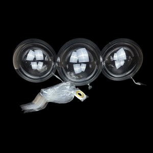 May include: Three clear, spherical, inflatable balloons made of transparent material. The balloons are round and smooth, featuring a reflective surface. A bundle of thin, clear plastic sticks and a small roll of adhesive tape are included below.
