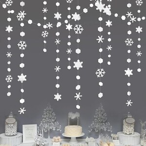 May include: White paper snowflake and geometric garland decorations hanging against a gray background. The garland features various snowflake designs and geometric shapes, creating a festive winter or holiday theme.