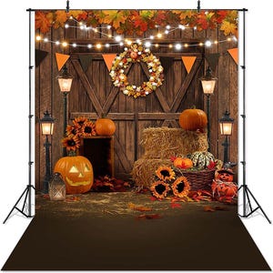 May include: A fall-themed backdrop featuring a rustic barn door, pumpkins, sunflowers, and hay bales. The scene is decorated with orange and black pennant flags, a wreath, and string lights. A jack-o'-lantern is also present, creating a festive atmosphere.