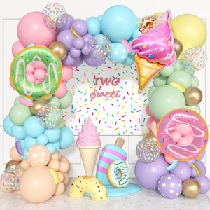 May include: A colorful balloon arch and decorative elements for a birthday celebration. The arch features pink, blue, green, and purple balloons, with donut and ice cream-shaped foil balloons. The backdrop reads "Two Sweet".