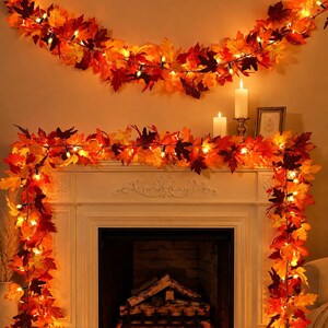 May include: A decorative garland featuring artificial autumn maple leaves in shades of red, orange, and yellow, illuminated by small warm white string lights. The garland is draped across the top and sides of a white fireplace mantel.