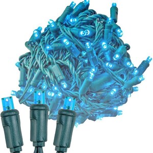 May include: A coiled strand of decorative string lights featuring numerous small, bright blue LED bulbs attached to a dark green wire. The lights are bundled together in a dense cluster, with three individual bulb sockets extended in the foreground.