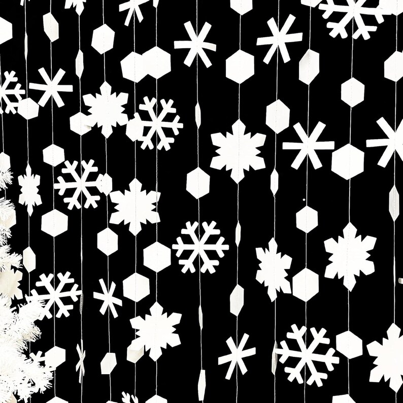 May include: White paper snowflakes and geometric shapes hang from strings against a black background. The decorations vary in size and shape, creating a festive, wintery display. Ideal for holiday decor.