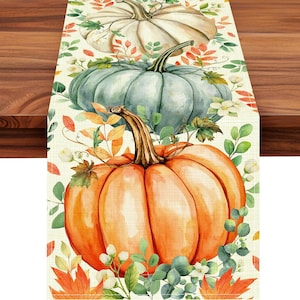 May include: A rectangular table runner featuring a repeating pattern of three pumpkins in white, sage green, and bright orange. The design includes watercolor-style autumn leaves in shades of red, orange, and green, along with small white flowers.