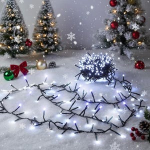 May include: A cluster of bright white LED string lights with a dark green wire, arranged in a coiled bundle with a long strand extending across a snowy surface, featuring small glowing bulbs spaced evenly along the flexible cord.