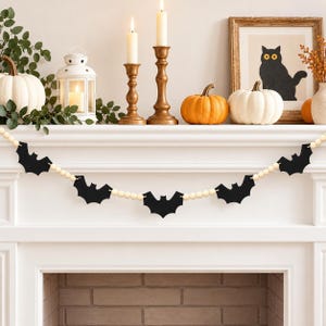 May include: A decorative garland featuring alternating black felt bat cutouts and natural light-colored wooden beads strung together. The garland is draped horizontally, showcasing five distinct bat shapes separated by segments of round wooden beads.