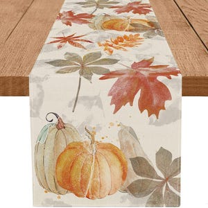 May include: A rectangular table runner featuring a printed pattern of autumn leaves in shades of orange, red, and muted green, interspersed with illustrations of pumpkins and gourds on a cream-colored fabric background with a textured appearance.