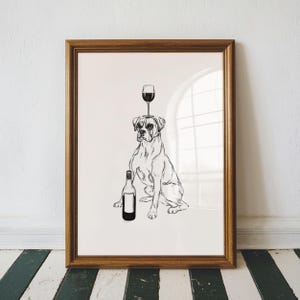 May include: A framed black and white print featuring a Boxer dog with a wine glass balanced on its head and a wine bottle beside it. The artwork is in a wooden frame and is displayed against a white wall.