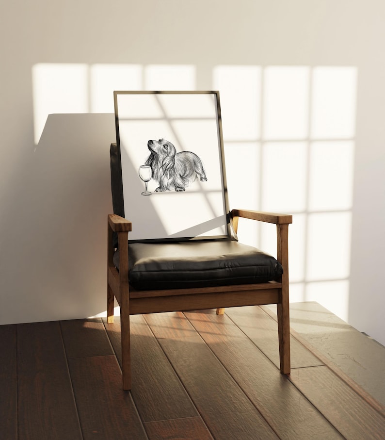 May include: A black and white pencil drawing of a dachshund dog holding a wine glass. The drawing is framed and sitting on a wooden chair with a black leather seat.