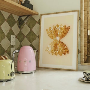 May include: A pink electric kettle with a silver handle and spout, a yellow toaster, and a framed print of a gold bow tie pasta shape on a white countertop.