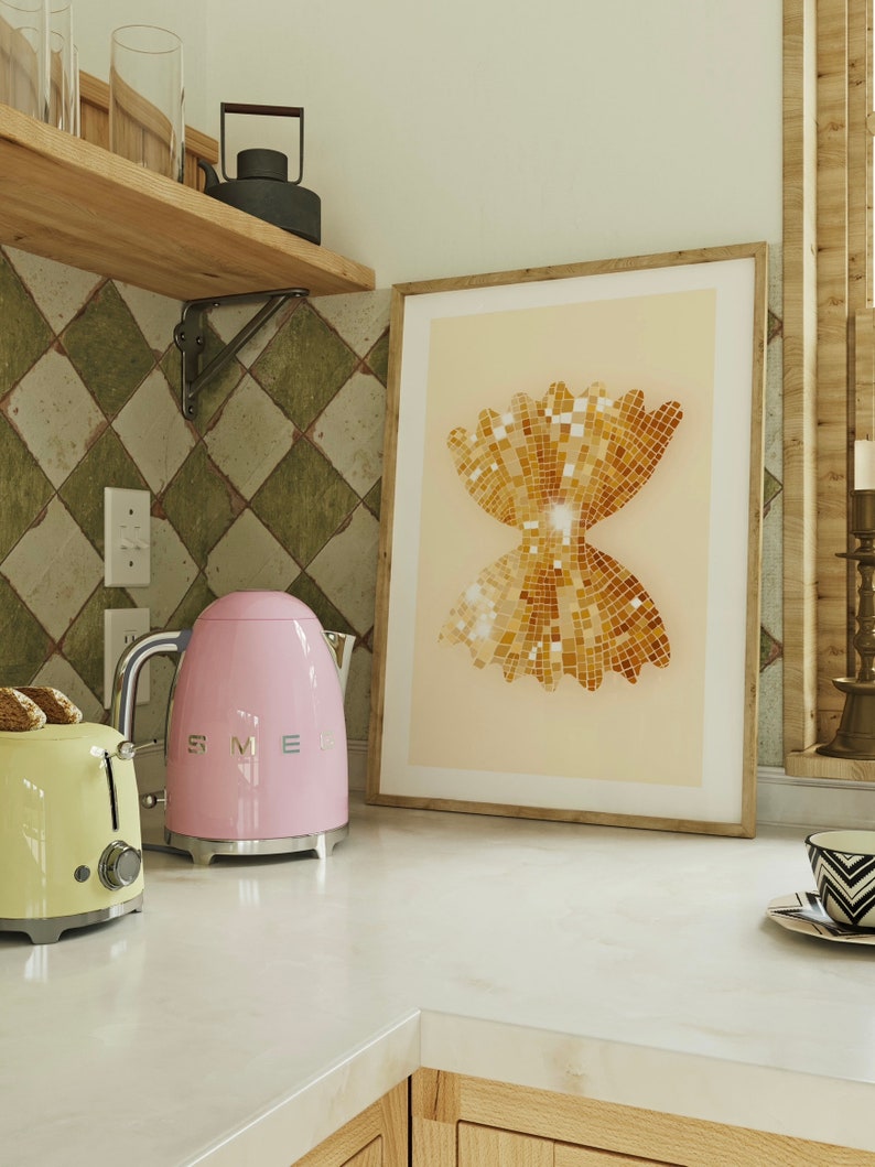 May include: A pink electric kettle with a silver handle and spout, a yellow toaster, and a framed print of a gold bow tie pasta shape on a white countertop.