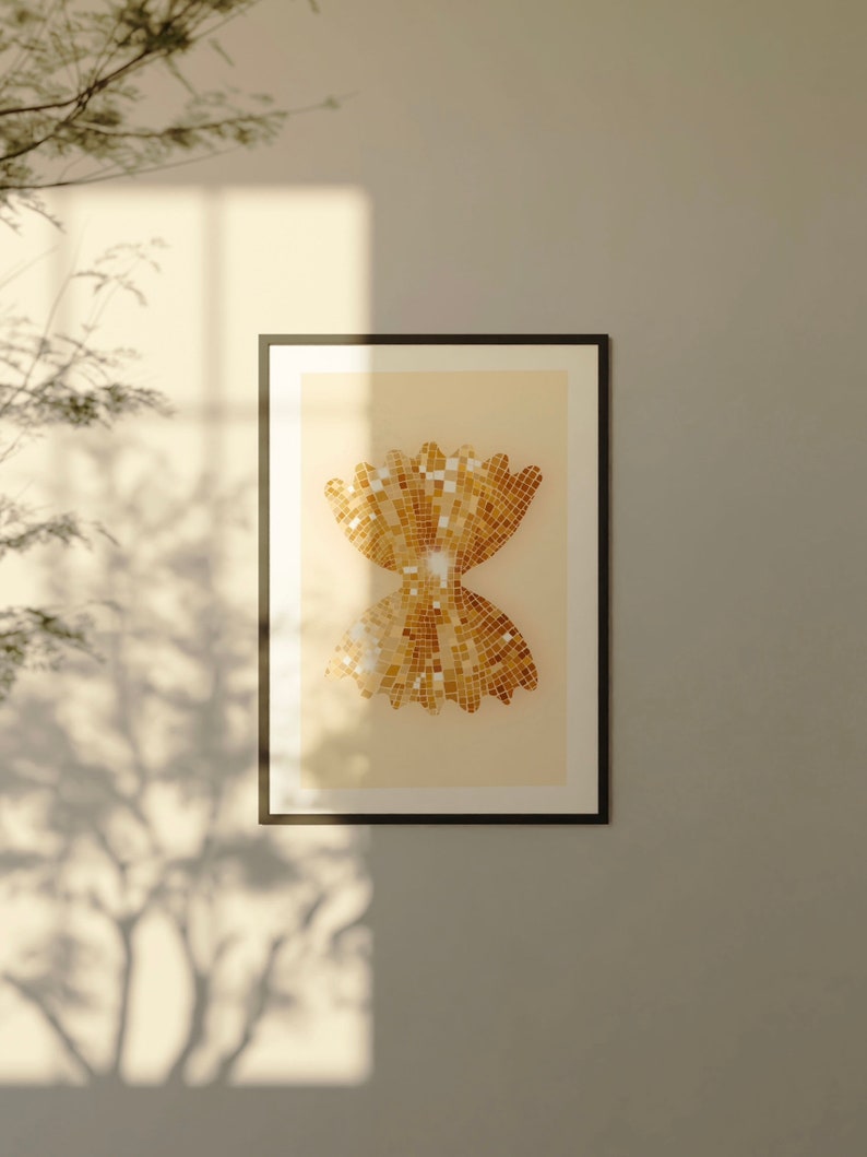 May include: A framed print of a gold mosaic design in the shape of a bow tie. The design is on a light beige background.