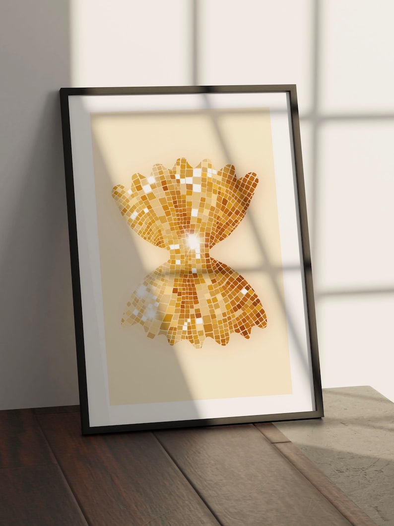 May include: A framed print of a gold glitter bow tie shape on a cream background.