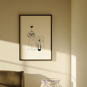 May include: Black framed art print featuring a line drawing of a dog with a wine glass balanced on its head and a wine bottle next to it. The artwork is displayed on a light-colored wall.