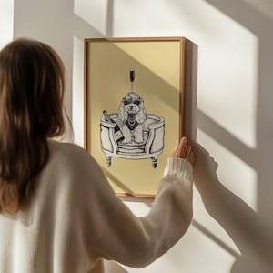 May include: A framed illustration of a dog wearing sunglasses and sitting in a plush dog bed with a bottle of champagne and a glass. The background is a light yellow colour.