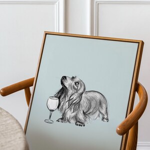May include: A framed black and white illustration of a dachshund dog holding a wine glass. The dog is looking up and the background is a light blue color.